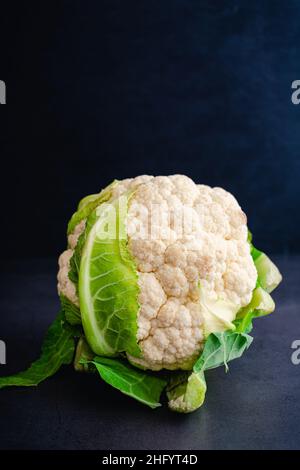 Ganzer Blumenkohl-Kopf auf dunklem Hintergrund: Ein ganzer Blumenkohl-Kopf mit noch einigen Blättern Stockfoto