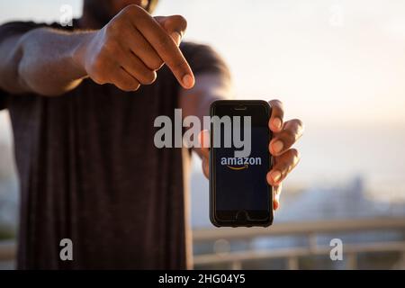 Ein Mann hält ein Smartphone mit dem Amazon-Logo. Ist ein US-amerikanisches multinationales Technologieunternehmen, das sich auf E-Commerce, Cloud-Computing und digitale e konzentriert Stockfoto