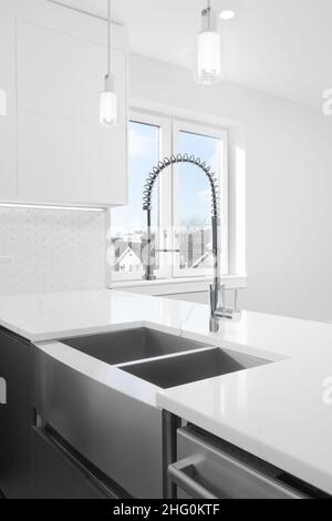 Ein Spülbecken aus Edelstahl mit Marmorablagefläche, Chromhahn und Blick auf ein leeres Wohnzimmer. Stockfoto