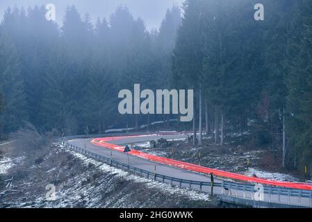 Leichte Wege von den Schlusslichtern auf einer kurvenreichen Alpenstraße durch einen Pinienwald in einer nebligen Winternacht Stockfoto