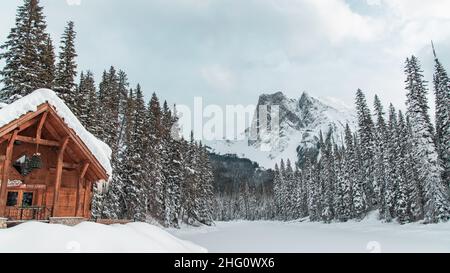 Yoho National Park, Kanada - 23 2021. Dez.: Holzhütte und cabane an der Seite des Frozen Emerald Lake, versteckt im Winterwald, umgeben von rockies Mount Stockfoto