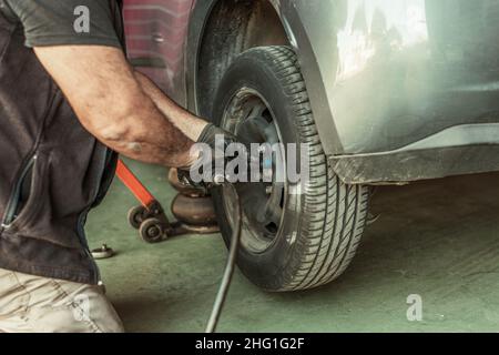 Mechaniker mit einem elektrischen Schraubendreher, um ein Rad in einer Garage zu entfernen Stockfoto