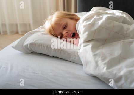 Das Kind liegt im Bett und gähnt Stockfoto