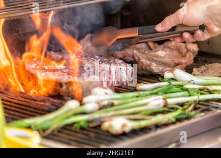 Rohes New York Steak auf dem Grill mit Flammen und Frühlingszwiebeln geröstet Stockfoto