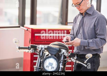 Techniker überprüft Elektromotorrad mit Smartphone in der Werkstatt Stockfoto