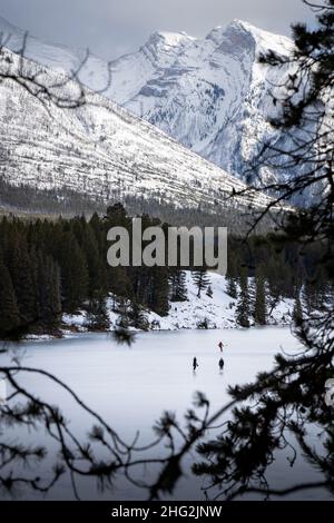 Eishockeyspieler und Schlittschuhläufer beim Schlittschuhlaufen auf einem gefrorenen Bergsee im Banff National Park. Stockfoto