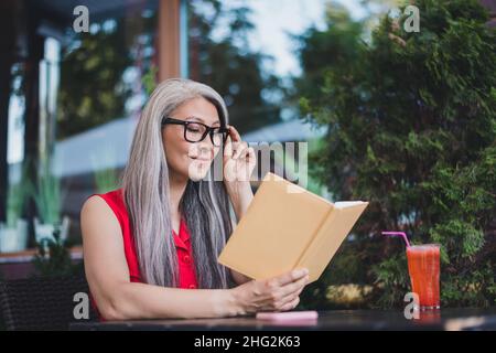 Porträt einer attraktiven, fröhlich fokussierten grauhaarigen Frau, die im Café im Freien ein Oranisiertagebuch liest Stockfoto