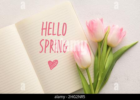 Notizbuch mit Text HALLO FRÜHLING und Tulpenblüten auf hellem Hintergrund Stockfoto