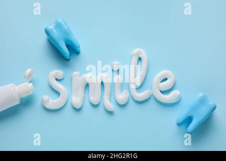 Geöffnete Tube und Wort LÄCHELN mit Zahnpasta auf blauem Hintergrund geschrieben Stockfoto