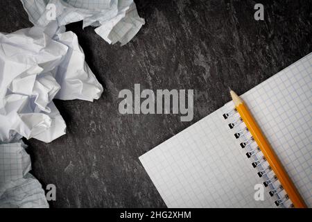 Zerknittertes und zerrissenes Papier auf dem Tisch. Zerrissenes Notizbuch. Papiermüll. Voller Korb mit Notizen. Notizblock und Bleistift auf zerknittertem Papierhintergrund. Stockfoto