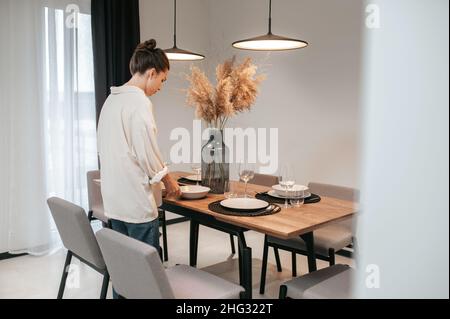 Junge Frau in einem swhite Hemd, die Teller auf den Tisch legt Stockfoto