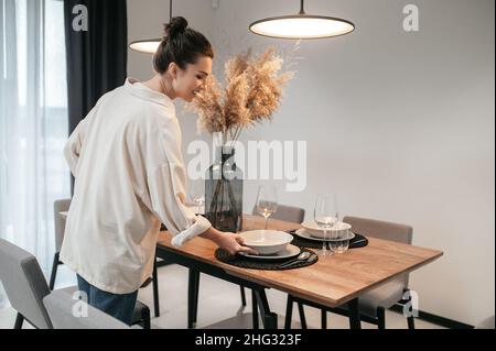 Junge Frau in einem swhite Hemd, die Teller auf den Tisch legt Stockfoto