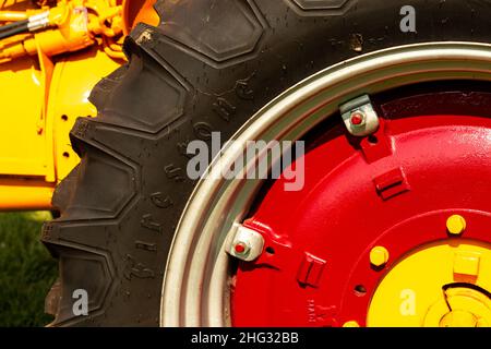 Ein schwarzer Firestone-Gummireifen, der auf einem roten und gelben Traktorrad montiert ist. Stockfoto