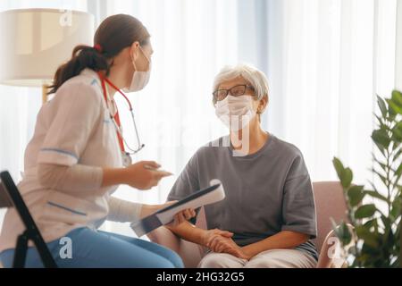 Arzt und ältere Frau mit Gesichtsmasken während des Coronavirus- und Grippeausbruchs. Virenschutz. COVID-2019. Masken übernehmen. Stockfoto