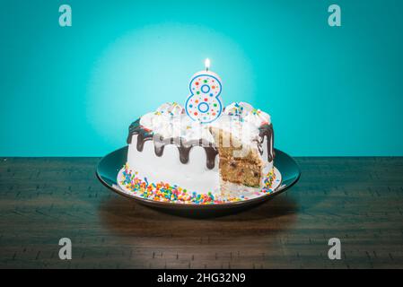Eine Geburtstagstorte, die eine Scheibe fehlt, trägt eine Kerze in Form der Zahl 8. Stockfoto