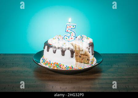 Eine Geburtstagstorte, die eine Scheibe fehlt, trägt eine Kerze in Form der Zahl 5. Stockfoto