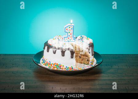 Eine Geburtstagstorte, die eine Scheibe fehlt, trägt eine Kerze in Form der Zahl 1. Stockfoto