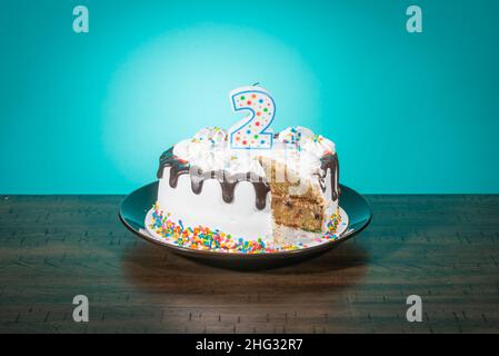 Eine Geburtstagstorte, die eine Scheibe fehlt, trägt eine Kerze in Form der Zahl 2. Stockfoto