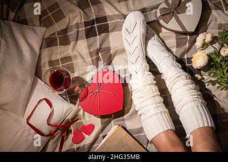 Valentinstag Feier flach lag mit Geschenk in herzförmigen Box und Womans Beine in weißen Socken auf Bett oder Boden Hintergrund, Draufsicht Stockfoto