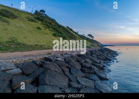 Wellenbrecher und grasbewachsener Hügel mit Bäumen bei Sonnenuntergang in Frankston, Australien Stockfoto