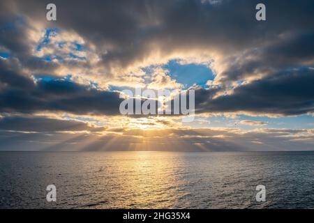 Minimalistische Meereslandschaft bei Sonnenuntergang mit Sonnenstrahlen, die durch Wolken ragen Stockfoto