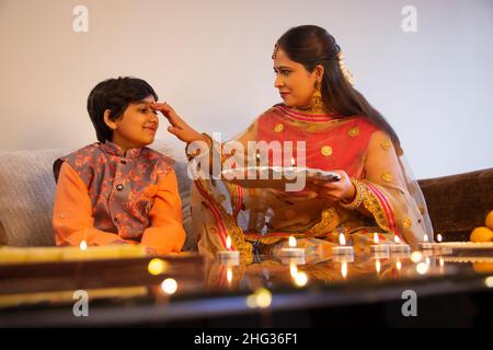 Indische Frau, die anlässlich von Diwali tika auf die Stirn ihres Sohnes auftrug Stockfoto