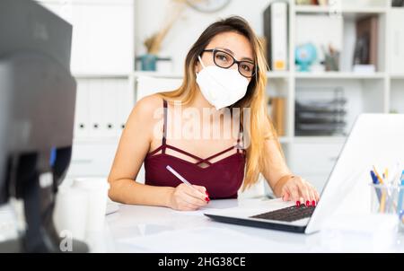 Latina Frau in Gesichtsmaske arbeitet im Büro Stockfoto