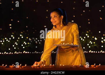 Junges Mädchen, das Diyas auf der Terrasse anläßlich von Diwali platziert Stockfoto