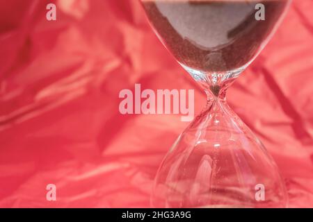 Sanduhr auf einem rot gewellten Seidenhintergrund. Luxus- und Zeitkonzept. Nichts ist ewig. Der Sand fließt durch die Glasbirnen der Uhr. Pl Stockfoto