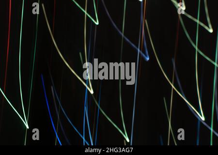 Helle mehrfarbige diagonale V-förmige Blendstrahlen auf Schwarz in kühlen Tönen. Banner mit abstraktem dunklem Hintergrund. Stockfoto