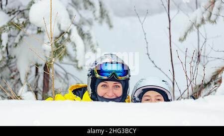 Junge Frauen aus dem Kaukasus und ihre Tochter verbringen gemeinsam Zeit in einem Snowboardpark. Mutter und Tochter in Helm und Brille