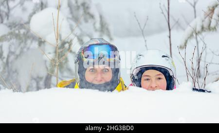 Junge Frauen aus dem Kaukasus und ihre Tochter verbringen gemeinsam Zeit in einem Snowboardpark. Mutter und Tochter in Helm und Brille