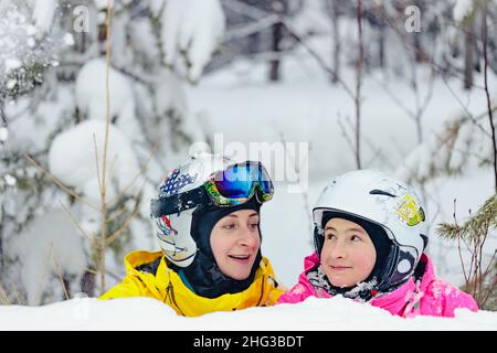 Eine fröhliche Frau und ihre Tochter verbringen gemeinsam Zeit im Snowboardpark. Mutter und Tochter der kaukasischen Ethnie in Helm und Brille Stockfoto