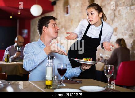 Wütender Mann, der sich bei der sich entschuldigenden Kellnerin über das Essen im Restaurant beschwerte Stockfoto