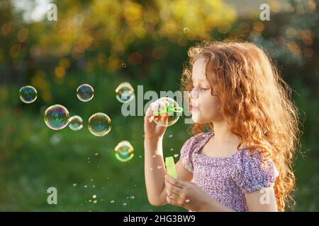 Niedliche kleine lockige Mädchen bläst Seifenblasen im Sommer Park. Gesundes Konzept. Stockfoto