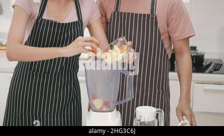 Happy Asian schöne junge Familie Paar Mann und Frau machen frischen Smoothie in der Küche zusammen zu Hause. Der Mann und die Frau gießen den gehackten Apfel Stockfoto
