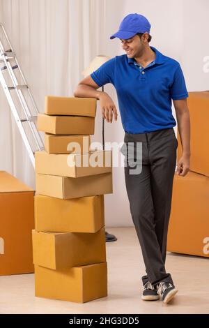 Delivery Boy in Uniform stehend mit gelehnt auf Pappkartons Stockfoto