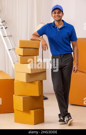 Delivery Boy in Uniform stehend mit gelehnt auf Pappkartons Stockfoto