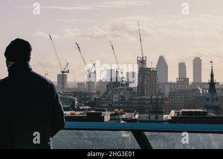 Ein Mann blickt von einem Aussichtspunkt in London, Großbritannien, auf Hochhausbüros und Bauarbeiten an der Skyline von London. Stockfoto