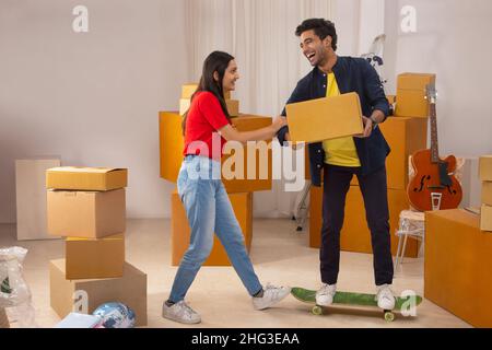 Junge mit Karton, der auf dem Skateboard steht, und Mädchen, das seine Hand hält Stockfoto