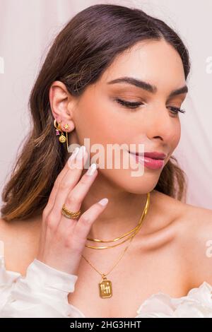 Nahaufnahme einer schönen jungen Frau mit goldener Halskette, zwei goldenen Schlangenketten, goldenen Ringen und goldenen Ohrringen. Schönes geschenk zum valentinstag. Stockfoto