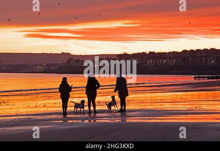 Portobello, Edinburgh, Schottland, Großbritannien 18th. Januar 2022. Atemberaubender Sonnenaufgang am Meer mit einer Temperatur von 1 Grad Celsius für diejenigen, die am Sandstrand trainieren. Im Bild: Menschen aus Hund, die am Ufer des Firth of Forth spazieren gehen. Kredit: Archwhite/alamy Live Nachrichten. Stockfoto