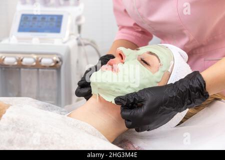 Die Kosmetikerin entfernt im Spa-Salon eine Tonmaske vom Gesicht einer jungen Frau. Schöne junge Mädchen bei der Kosmetikerin macht die Spa-Verfahren Stockfoto
