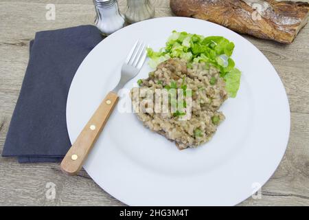 Pilzrisotto auf einem weißen Teller auf einem Holztisch mit Salat Stockfoto