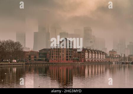 London, Großbritannien. 18th Januar 2022. Wetter in Großbritannien: Am frühen Morgen werden Nebel und Wolken langsam über den Gebäuden des Gewerbeparks Canary Wharf sichtbar, die vom Greenland Dock aus gesehen werden. Kredit: Guy Corbishley/Alamy Live Nachrichten Stockfoto