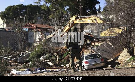 Jerusalem, Israel. 17th Januar 2022. Ein Mitglied der israelischen Sicherheitskräfte steht Wache, als ein Baggergrabator eine Struktur in der Baumschule des Familienhauses eines Palästinensers, Salhiya, abreißen lässt, die am 17. Januar 2021 in Jerusalem, Israel, im Scheich-Jarrah-Viertel geräumt werden soll. Salhiyas Familie ist seit 2017 mit einer Räumungsdrohung konfrontiert, als das Land, in dem sich sein Haus befindet, für den Schulbau bestimmt wurde. Das palästinensische Viertel Sheikh Jarrah ist derzeit das Zentrum einer Reihe von Eigentumsstreitigkeiten zwischen Palästinensern und rechtsgerichteten jüdischen Israelis. Einige h Stockfoto