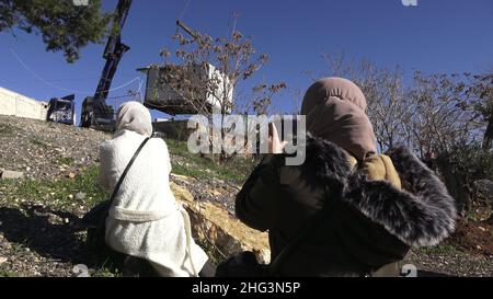 Jerusalem, Israel. 17th Januar 2022. Palästinensische Frauen beobachten, wie ein Kran eine Struktur auf dem Gelände des Familienhauses einer Palästinenserin, Salhiya, hochhebt, die am 17. Januar 2021 in Jerusalem, Israel, im Scheich-Jarrah-Viertel geräumt werden soll. Salhiyas Familie ist seit 2017 mit einer Räumungsdrohung konfrontiert, als das Land, in dem sich sein Haus befindet, für den Schulbau bestimmt wurde. Das palästinensische Viertel Sheikh Jarrah ist derzeit das Zentrum einer Reihe von Eigentumsstreitigkeiten zwischen Palästinensern und rechtsgerichteten jüdischen Israelis. Einige Häuser wurden von israelischen Siedlern besetzt Stockfoto