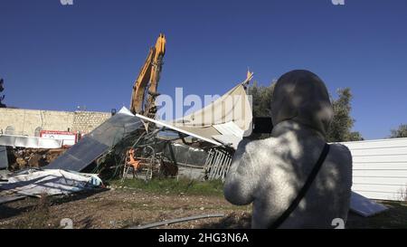 Jerusalem, Israel. 17th Januar 2022. Eine Palästinenserin fotografiert einen Bagger, der eine Struktur auf dem Gelände des Familienhauses eines Palästinensers, Salhiya, zerstört, die am 17. Januar 2021 in Jerusalem, Israel, im Scheich-Jarrah-Viertel geräumt werden soll. Salhiyas Familie ist seit 2017 mit einer Räumungsdrohung konfrontiert, als das Land, in dem sich sein Haus befindet, für den Schulbau bestimmt wurde. Das palästinensische Viertel Sheikh Jarrah ist derzeit das Zentrum einer Reihe von Eigentumsstreitigkeiten zwischen Palästinensern und rechtsgerichteten jüdischen Israelis. Einige Häuser waren besetzt Stockfoto