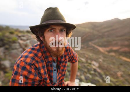 Porträt eines hübschen jungen bärtigen kaukasischen Mannes mit Hut auf dem Berggipfel Stockfoto