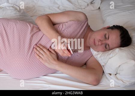 Kaukasische Frau mit Telefon, die zu Hause auf dem Sofa Wehen hat und atmet Stockfoto